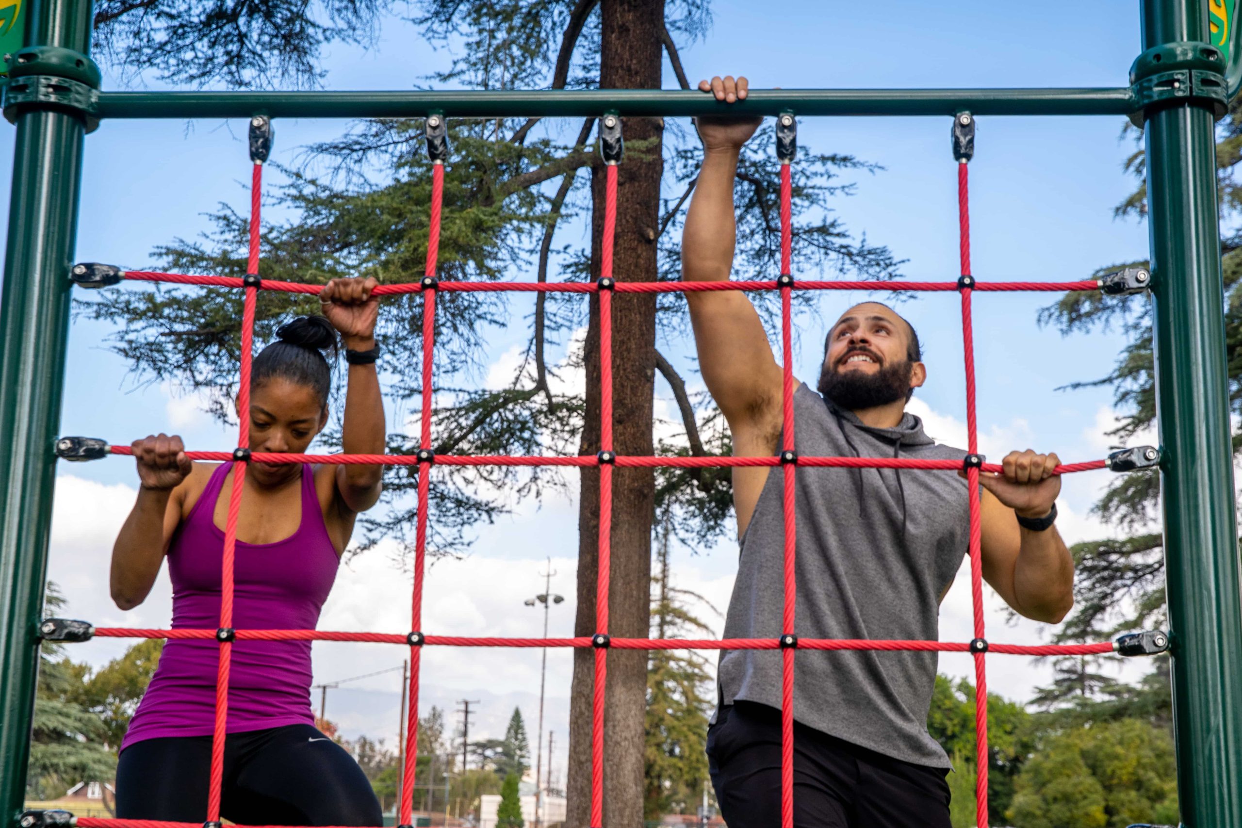 A man and a woman climbing the Cargo Net & Rope Climb in park.